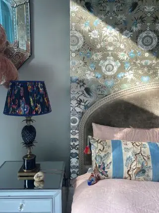 Dormitorio con papel tapiz encima de la cama, alcoba pintada de gris y mesita de noche con lámpara