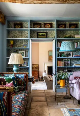 Salón con estantes alrededor de la puerta, sofá y sillón y suelo de piedra.