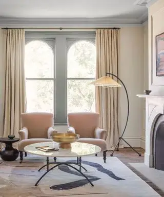 Moderní obývací pokoj s obloukovými okny, odpovídajícími lehátky, ladná stojací lampa, koberec, krb
