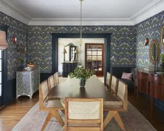 En spisestueidé med blå tapet med William Morris-trykk, stor mørk treskjenk og lyst tre spisebord med rottingstoler