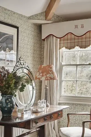 canto de um quarto com cortinas e sanefa, papel de parede verde, penteadeira com espelho, abajur, obra de arte, vaso, cadeira