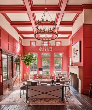 Ampio spazio abitativo con soffitto a doppia altezza, pareti e soffitto dipinti di rosso e rosa, posti a sedere attorno al camino