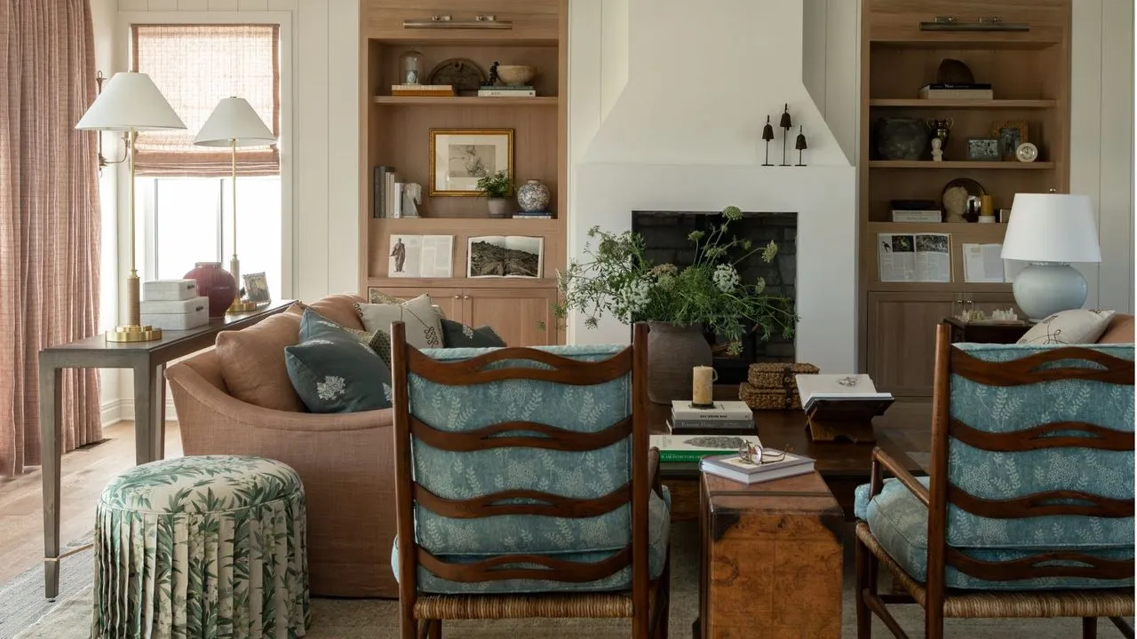 gårdshus møter bestemor elegant estetisk hvit stue med not og fjær vegger lys eik innebygd hyller peis myk rosa sofa skjørt floral ottoman og to mørkt tre lenestoler med blå puter' loading='lazy' title=