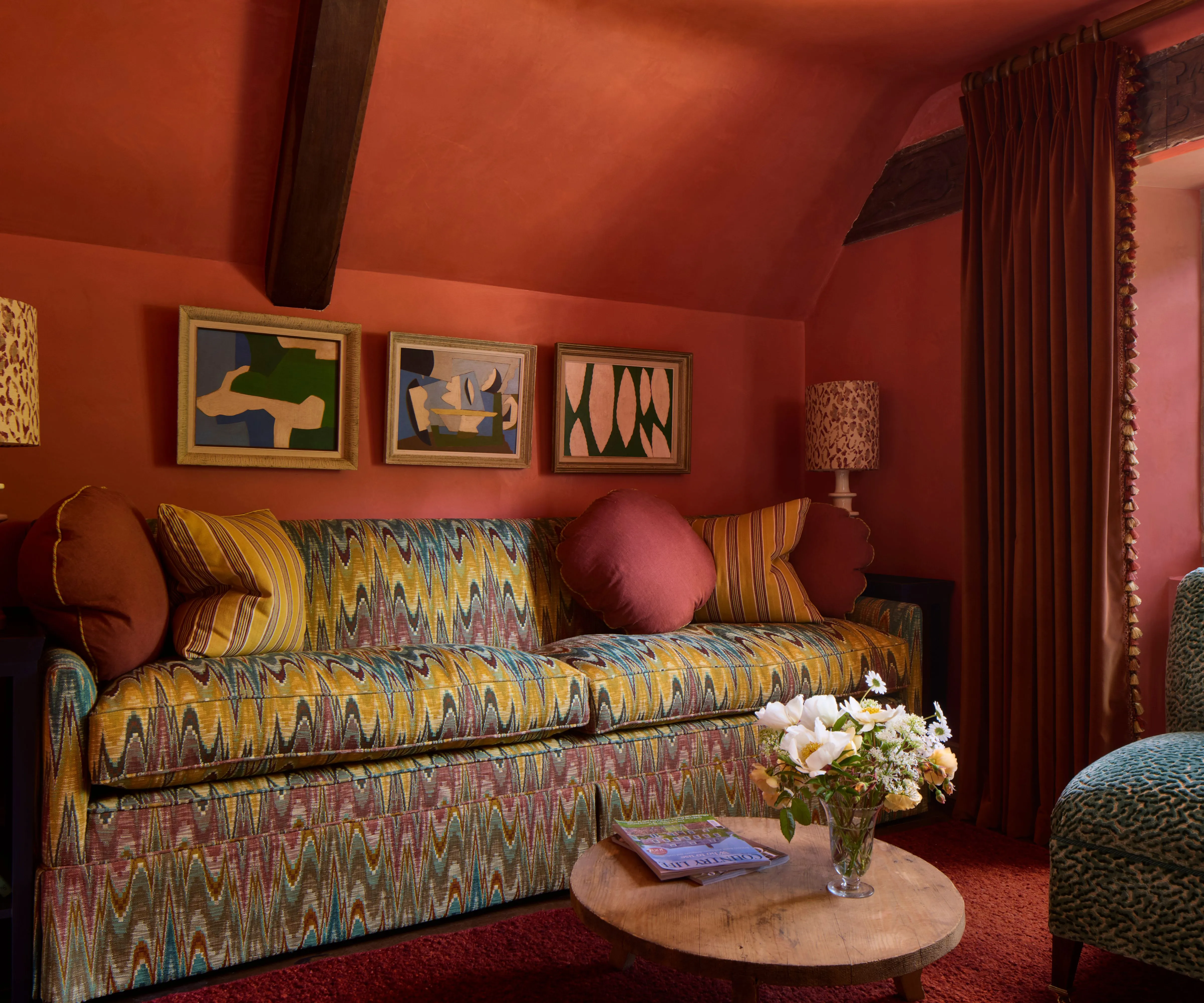 ciemnoczerwony pomarańczowy kolor salonu przesiąknięty bogatą kolorystyką, ozdobiony kanapą z nadrukiem w stylu Missoni z poduszkami w żółte paski i czerwonymi okrągłymi poduszkami' loading='lazy' title=