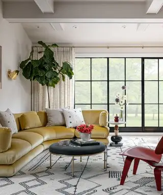 Salón con grandes ventanales y sofá de terciopelo curvo amarillo.