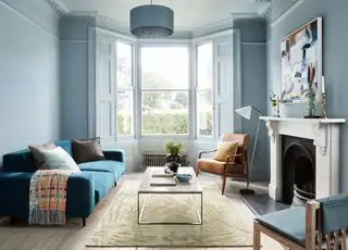 blå stue med vægge og træværk malet ensfarvet, trægulv, tæppe, blå sofa, sofabord, læderlænestol, pejs, kunstværk