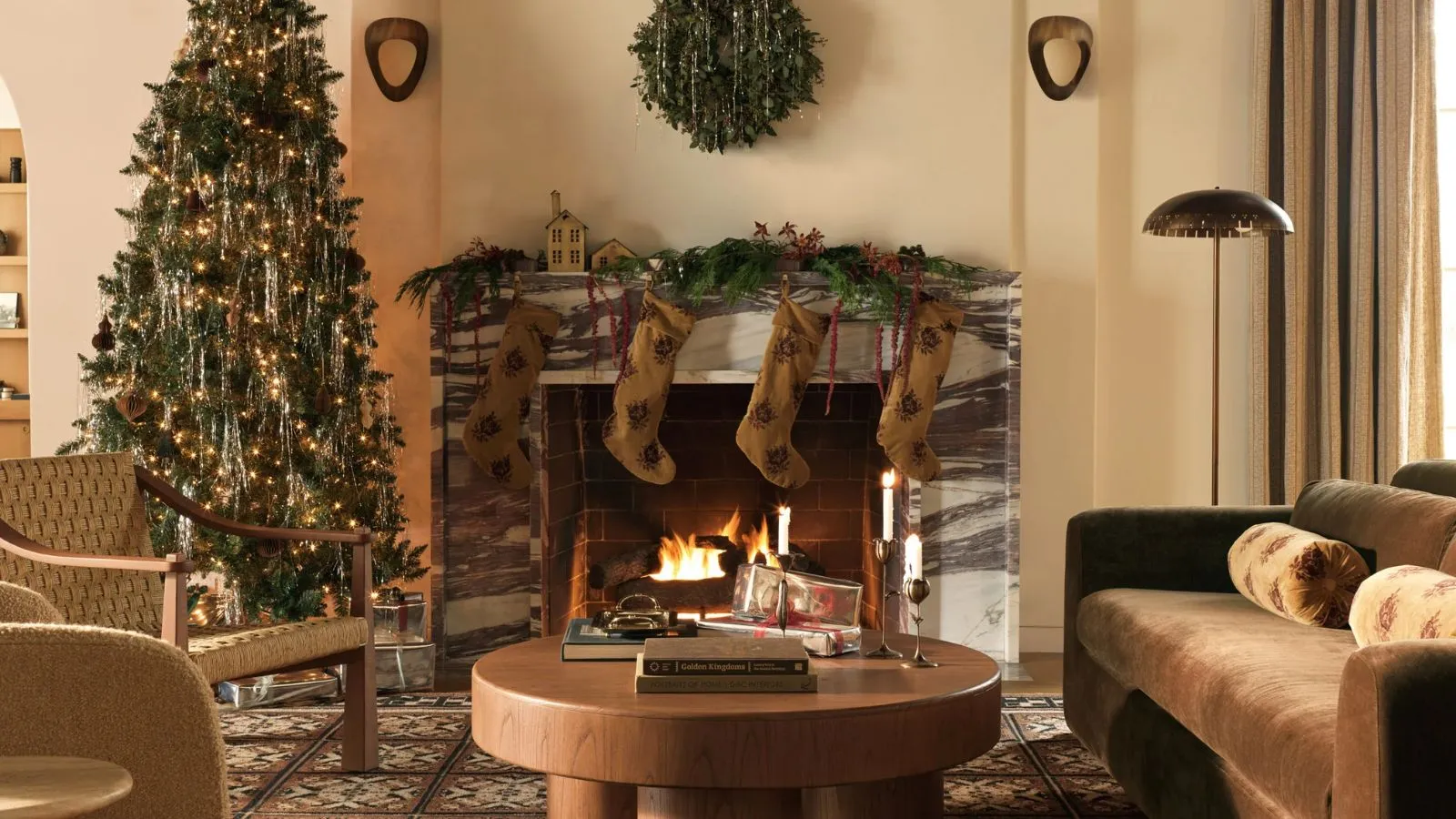 kampania Lulu i Gruzja Boże Narodzenie 2025 zdjęcia nastrojowego, ciepłego salonu z zapalonym marmurowym kominkiem ozdobionym girlandą aksamitne pończochy aksamitna kanapa stolik kawowy zielone fotele i choinka' loading='lazy' title=