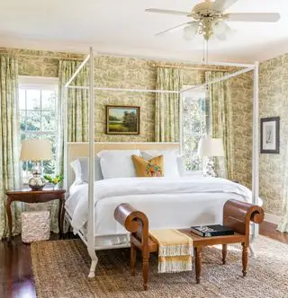 Dormitorio con cama con dosel blanca y papel tapiz floral verde y cortinas.