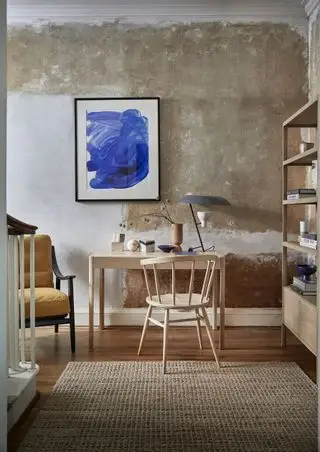 escritório em casa com mesa e cadeira de madeira clara clara, parede de gesso com textura áspera, arte em azul, unidade de armazenamento, poltrona, tapete texturizado em tons neutros