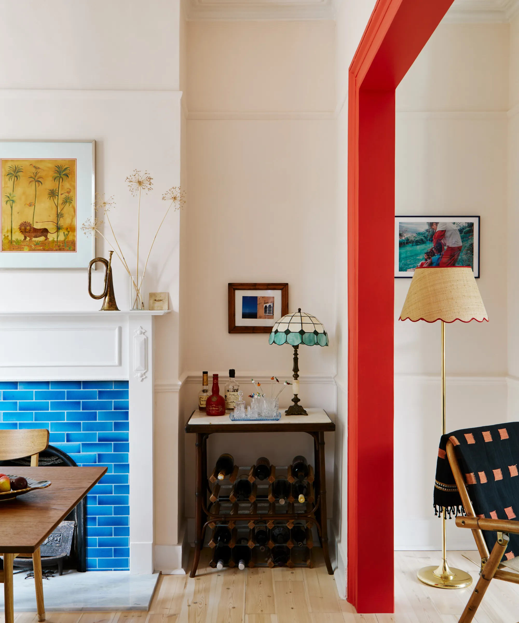 en knaldrød dørkarm, der adskiller to rum. Til venstre er en spisestue med en lyseblå flisebelagt pejs og en vinreol under et lille barbord.' loading='lazy' title=