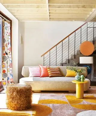 Sala de estar moderna y luminosa con un curvilíneo sofá color crema, mesa auxiliar amarilla, alfombras y cojines de colores