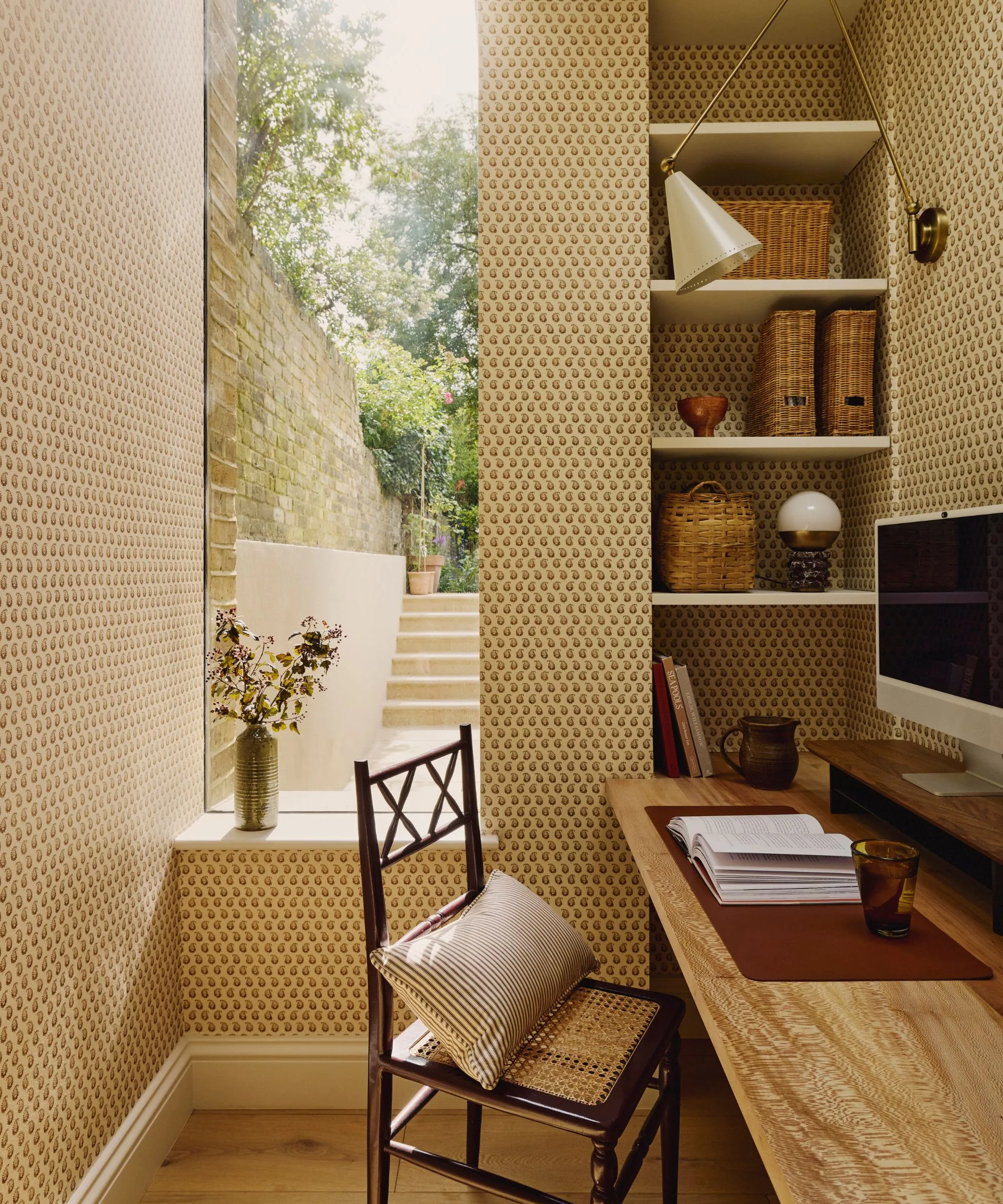 模様のある壁紙が貼られたオフィスエリア。棚の中に収納スペースがあり、その上に本とコンピューターが置かれた机が組み込まれています。' loading='lazy' title=