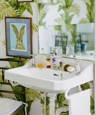 baño con papel pintado de hojas grandes y una lámina artística de conejito