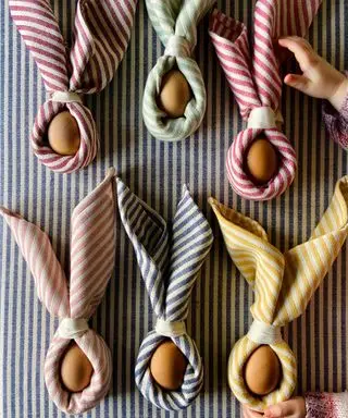 servilletas a rayas envueltas alrededor de huevos como orejas de conejo para una mesa de Pascua