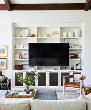 Innbydende hvit stue med mørke tredetaljer, stor oppbevarings- og displayenhet med tv, skinnstol, salongbord med blå tekstur og kremsofa