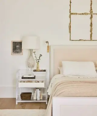chambre aux murs blanc chaud, lit et jeté rembourrés et sculpture en bronze au-dessus