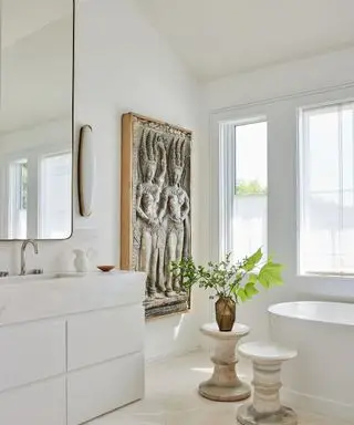 Salle de bains murs blancs œuvres d'art sculpturales en relief et deux tabourets sur pied