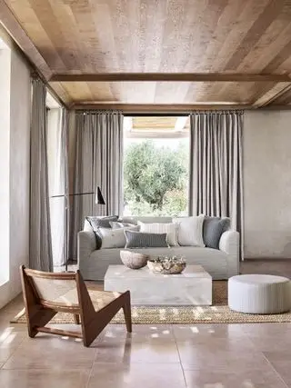 sala de estar neutra com vista externa, piso de pedra, sofá cinza, cadeiras de madeira, cortinas cinza, teto de madeira