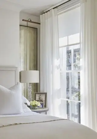 quarto branco com um toque claro e arejado, cortinas brancas, cama creme, quarto pequeno