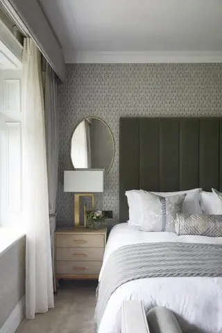 quarto cinza com papel de parede estampado cinza, cabeceira de veludo verde sálvia, roupa de cama branca, espelho dourado, abajur dourado, cortinas cinza