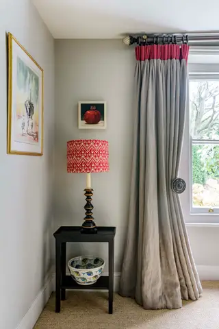 Grande janela com vista para o jardim verde, decorada com cortinas estampadas de folhas brancas e verdes, cadeira com manta amarela