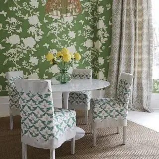 sala de jantar com papel de parede floral verde, mesa redonda branca, cadeiras brancas com tecido e cortinas com estampa neutra