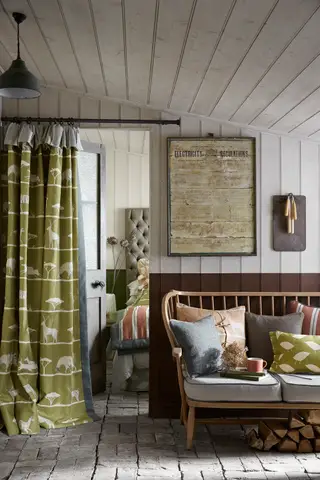 Quarto floral, maximalista e ousado com cortinas estampadas, papel de parede, estofados, cama decorada com cobertores e almofadas, sofá listrado creme com almofadas ao lado da janela