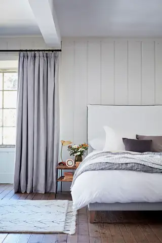 Quarto de estilo tradicional com cama grande, paredes pintadas de verde, lustre, tapete preto e creme, cômoda preta com espelho arredondado dourado acima, cortinas com estampas tropicais