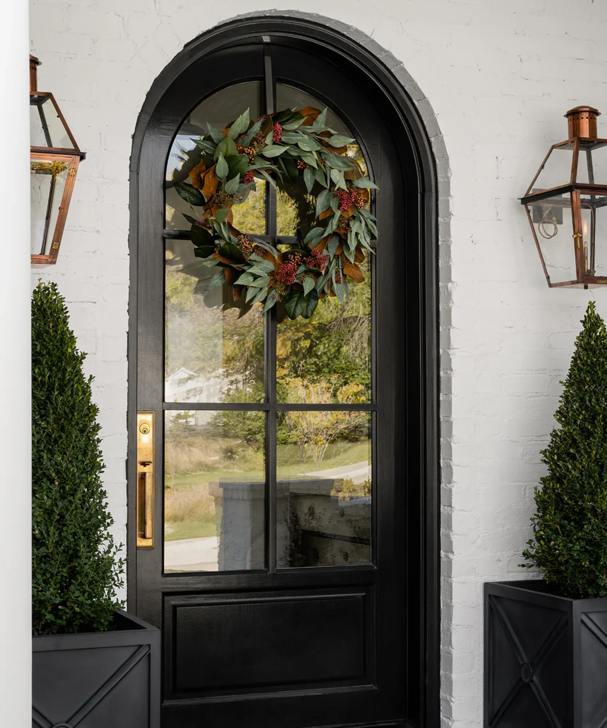 una porta d'ingresso nera da cui pende una ghirlanda di finto eucalipto' loading='lazy' title=