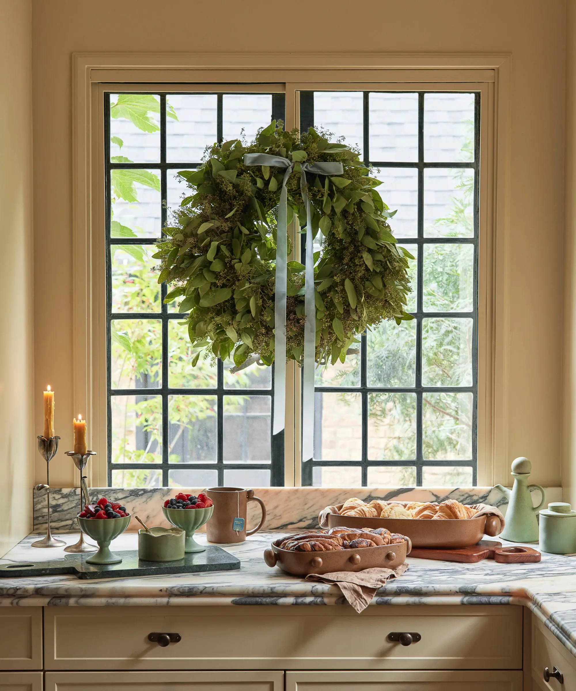 una cucina con il cibo sul piano di lavoro e una ghirlanda decorativa appesa alla finestra con un fiocco di nastro blu' loading='lazy' title=