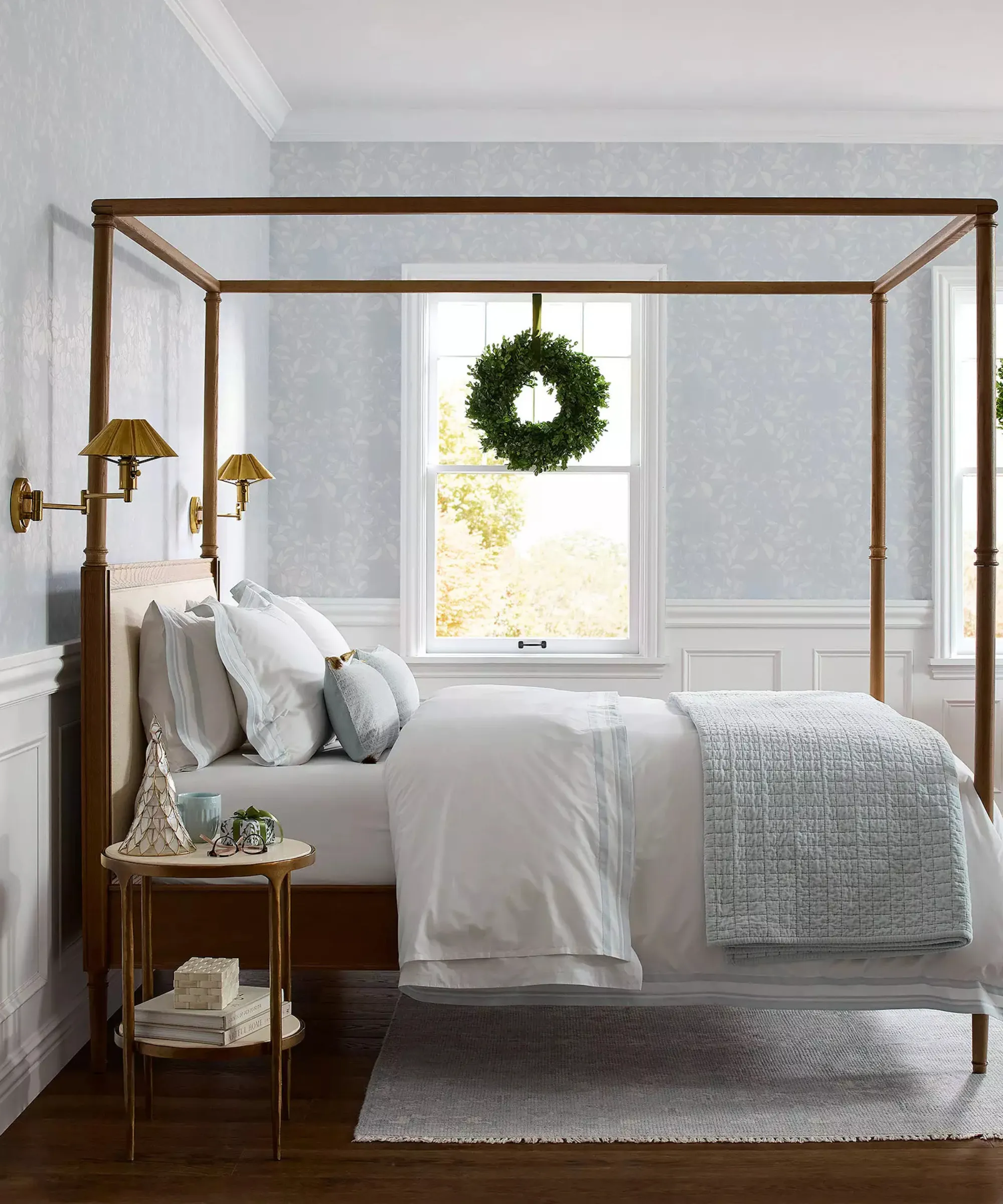 una camera da letto costiera con carta da parati blu, un letto con cornice in legno scuro, lenzuola azzurre e bianche e una ghirlanda appesa alla finestra' loading='lazy' title=