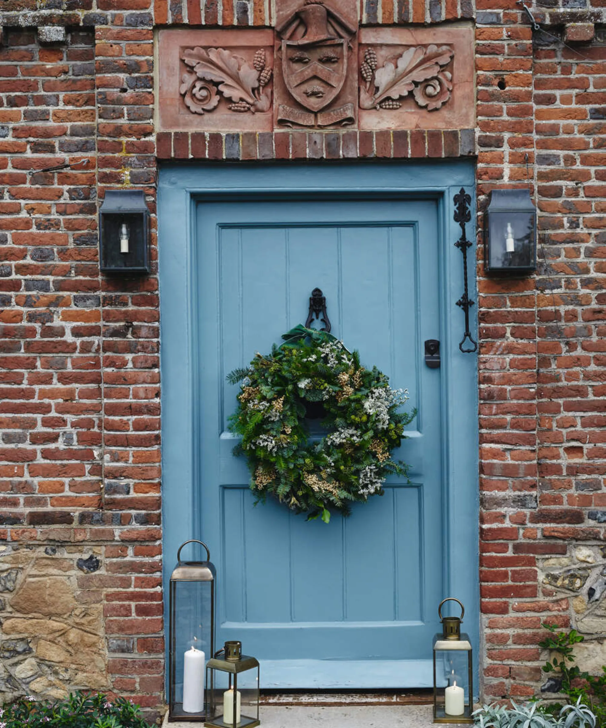 una casa di mattoni con una porta d'ingresso blu da cui pende una ghirlanda' loading='lazy' title=