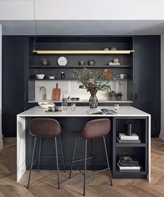 Cocina con suelo de madera, muebles empotrados en negro y crema, taburetes junto a la barra desayunadora, techos altos y molduras.