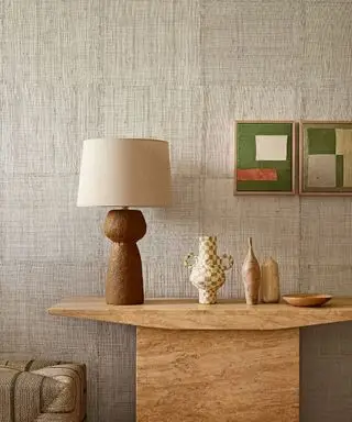 Papier peint neutre et texturé, finition crème, console en marbre, deux imprimés abstraits roses et verts, lampe de table haute avec base fluide et incurvée, abat-jour crème,