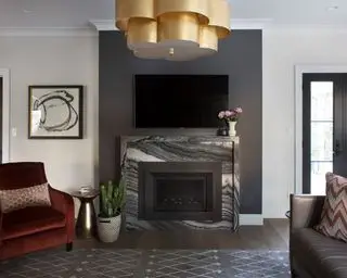Sala de estar moderna com lareira de mármore, TV montada nas paredes, paredes pintadas em creme, piso de madeira escura, luminárias suspensas douradas, obras de arte, assentos