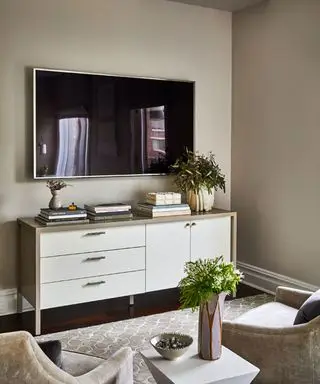 Sala moderna com TV de parede, aparador amplo e de madeira decorado com livros, flores e enfeites