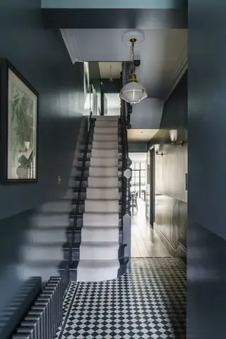 hall/entré med små grafiske svarte og hvite fliser, blekkblå vegger og malte trapper, trappeløper