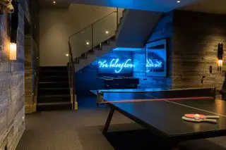 sala de jogos no porão com tênis de mesa, matraquilhos, obras de arte, revestimento de madeira e letreiro de néon, degraus para o andar de cima, luminárias de parede