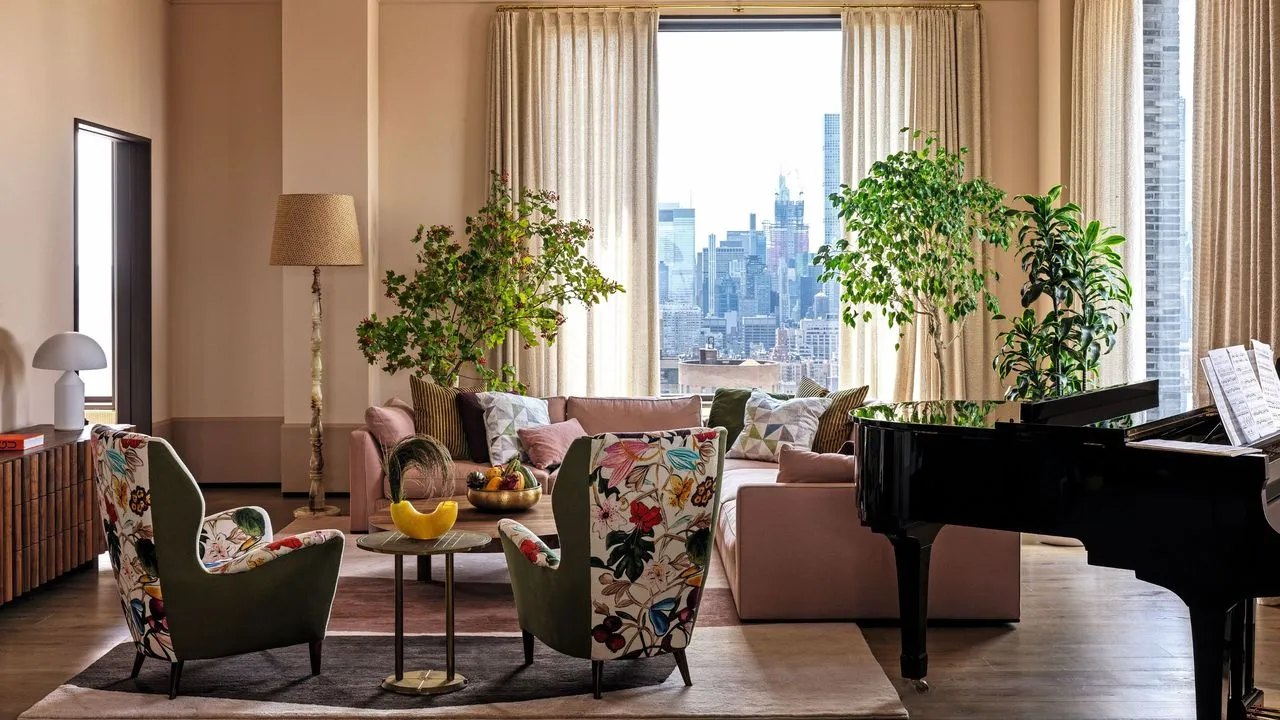 Salón con paredes de color rosa pálido y un sofá esquinero rosa con sillones estampados y un piano de cola en la esquina' loading='lazy' title=