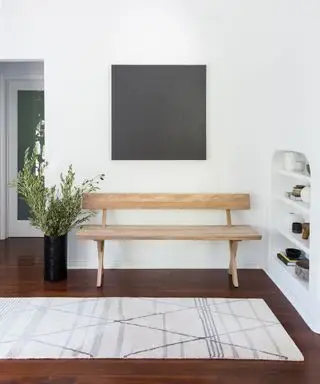 Moderner Eingangsbereich mit weißer Wand, dunklem Boden und Holzbank