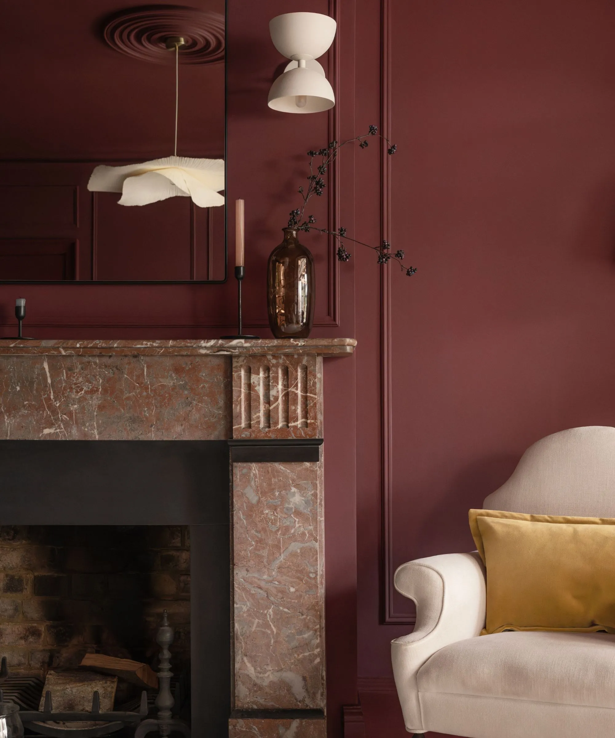 Obývacia izba s tmavočervenými stenami, mramorovým krbom so zrkadlom nad ním a béžovým kreslom s horčicovým vankúšom.' loading='lazy' title=