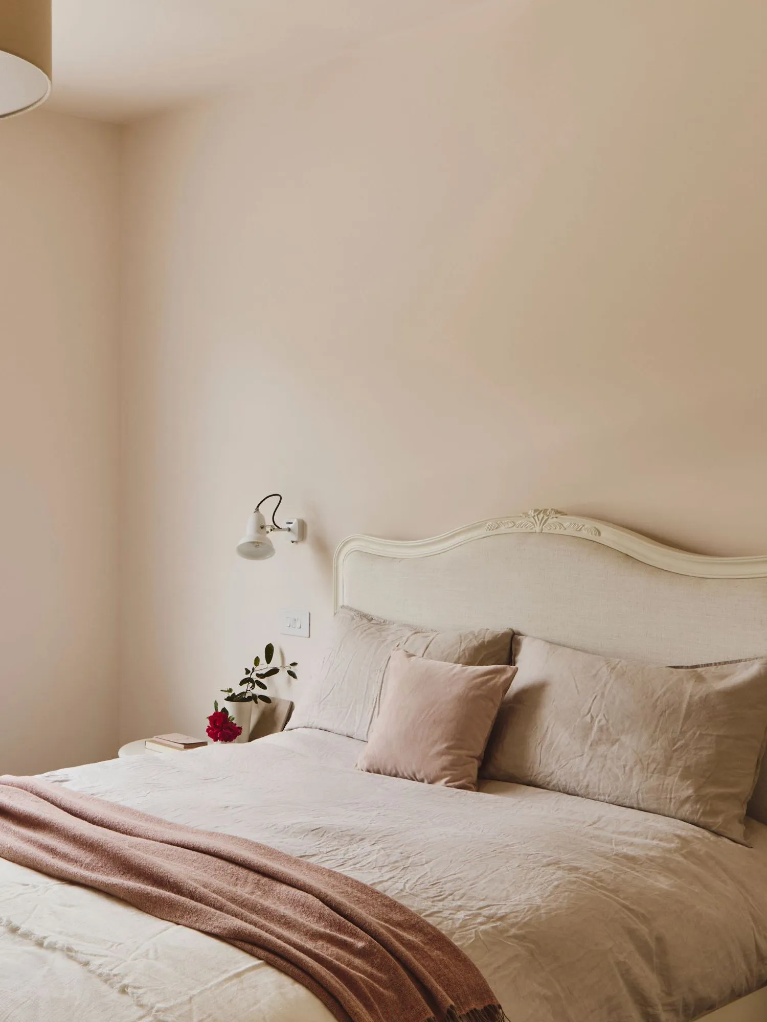 Spálňa so svetloružovými stenami s neutrálnou posteľnou bielizňou a veľkým oknom s rímskou roletou.' loading='lazy' title=
