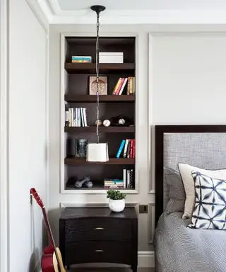 Ein Beispiel für Schlafzimmerbeleuchtungsideen, das ein monochromes Schlafzimmer mit eingebauten Regalen neben dem Bett zeigt