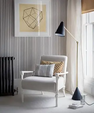 Ein Beispiel für Schlafzimmerbeleuchtungsideen mit einer schwarzen Stehlampe neben einem Sessel und einer gestreiften Tapete