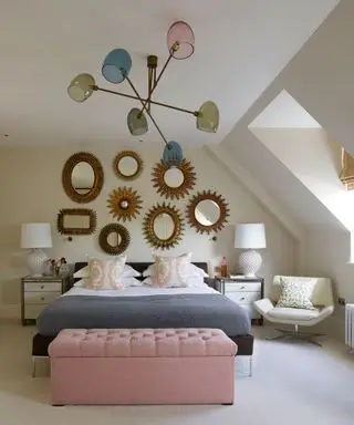 Ein Beispiel für Schlafzimmerbeleuchtungsideen, das eine übergroße bunte Deckenlampe in einem weißen Schlafzimmer mit einem blauen Bett vor einer Wand mit Spiegeln zeigt
