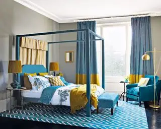 Ein blaues Schlafzimmer mit einem Himmelbett, gelben Akzenten und einer goldenen Stehlampe