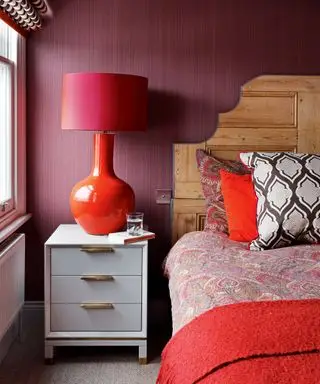 Ein Beispiel für Schlafzimmerbeleuchtungsideen, das ein Schlafzimmer mit roten Wänden und einer roten Tischlampe zeigt