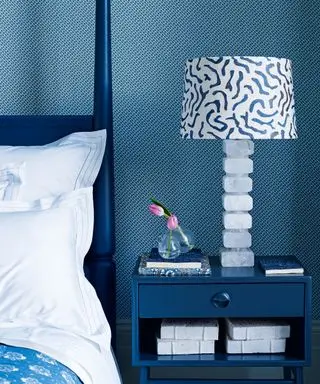 Ein Beispiel für Schlafzimmerbeleuchtungsideen, das eine Nahaufnahme eines blauen Schlafzimmers mit einem blauen Nachttisch und einer verzierten blau-weißen Tischlampe zeigt