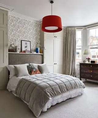 Ein neutrales Schlafzimmer mit einem großen Doppelbett mit Überwurf und Kissen unter einer roten Deckenlampe