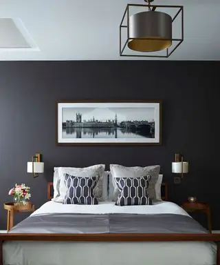 Ein Beispiel für Schlafzimmerbeleuchtungsideen, das eine dunkelgraue Wand hinter einem Bett mit weiß-grauer Bettwäsche und weißer Wandbeleuchtung zeigt